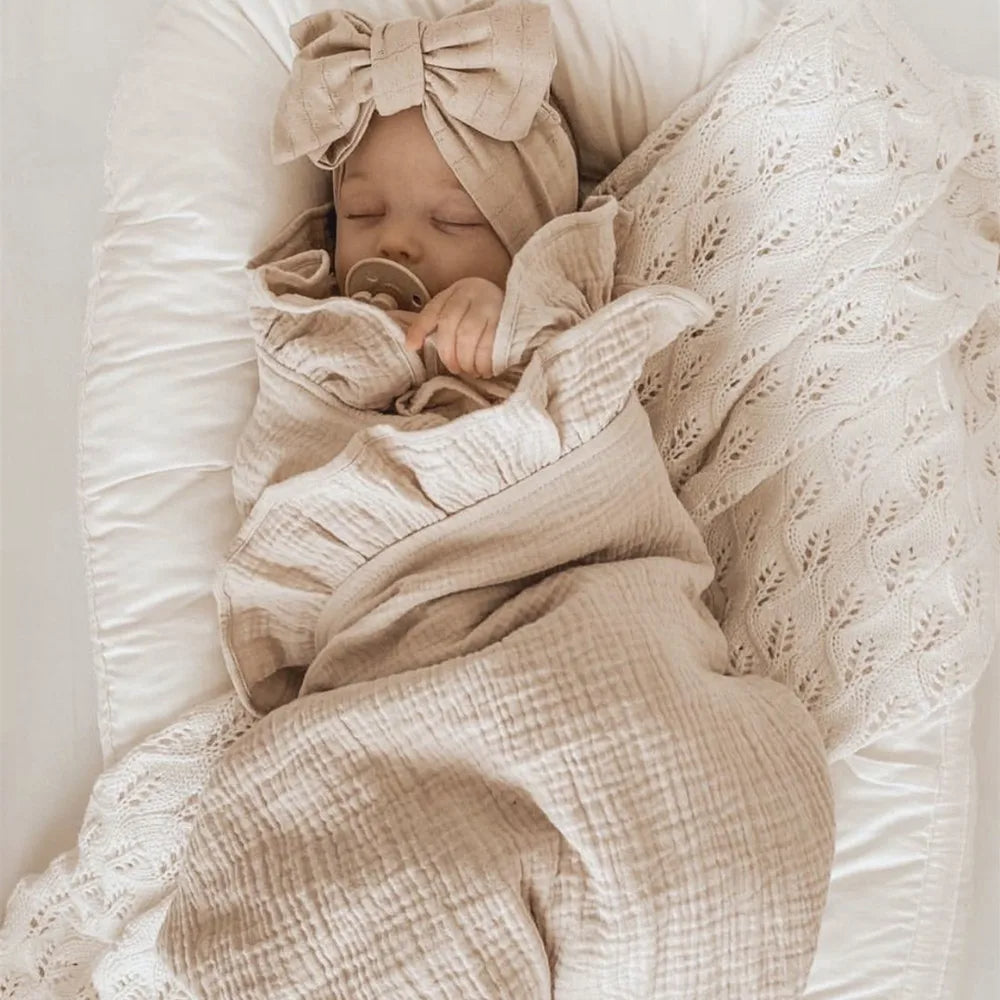 Couverture d'Emmaillotage Beige en Mousseline de Coton sur un bébé dormant sur un lit blanc