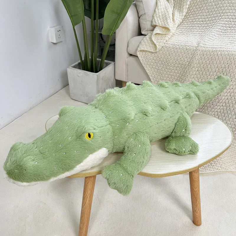 Doudou Géant Divertissant en Forme de Crocodile sur un table avec un canapé et une plante verte en fond